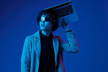 Portrait of a stylish male hacker with a laptop and futuristic glasses in blue light, cyber...