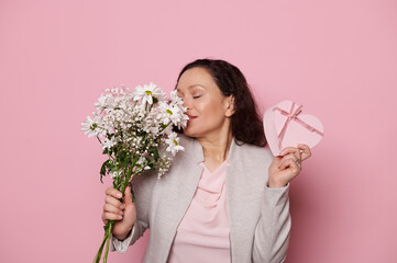 Delightful multi-ethnic middle-aged pretty brunette, sniffing the beautiful bouquet of...