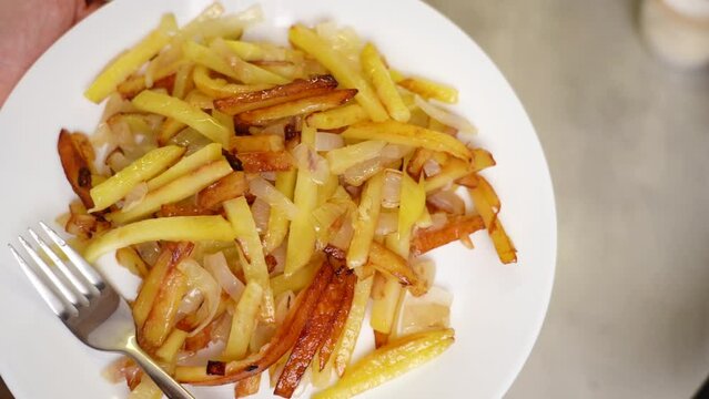 Fried golden potatoes in white plate with fork rotate. 