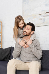 preteen girl hugging happy bearded father sitting on sofa in living room.