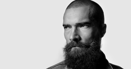 Brutal and stylish portrait of young man with beard on gray background. Artistic black and white photography. Guy with strong look and character.