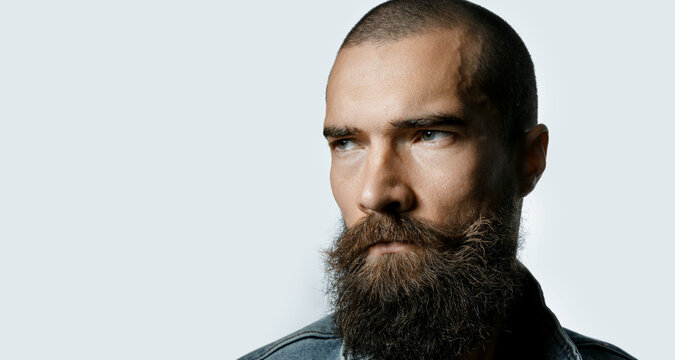 Brutal and stylish portrait of young man with beard on gray background. Guy with strong look and character.