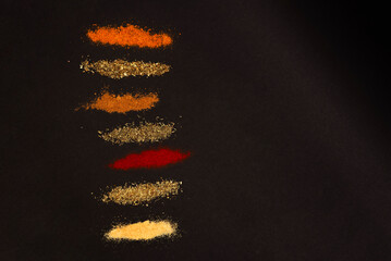 Spices scattered on a black background. Coriander, marjoram, paprika, thyme and rosemary, universal seasoning, garlic - heaped on a dark background.
