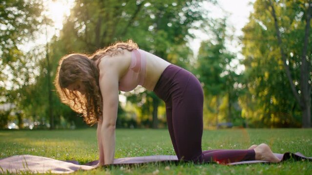 Fit Woman practising Sports in Park. Slim Fitness Girl doing Cat Cow Yoga Pose on Mat outdoors in Natural Environment. Stretching and Wellbeing and Connection with Nature. 4K wide orbit shot
