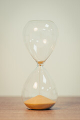 Sandglass on the white background, on wooden table, close up, vertical shot. Concept of passing time, deadline, minute and measure, toned image