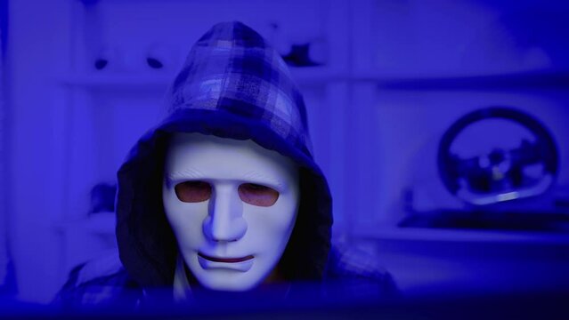 hacker wearing a white mask is using a computer to steal confidential information.Concepts: computer crime, burglary, business security on computer networks

