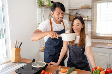 Happy asian couple cooking together in modern kitchen in morning.