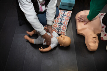 Three people practice first aid and CPR with an adult CPR manikin and another baby resuscitation...