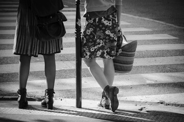 Parisian lifestyle. Two women wearing skirts waiting to cross street. Girl friends spend time together. Paris, France. Springtime mood in air. Black white historic photo