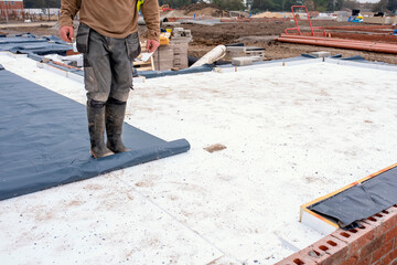 Builder placing polystyrene insulation boards on waterproofing membrane during floor construction....