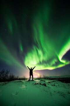 imagen de una aurora boreal en el cielo nocturno de Islandia, con las monta&ntilde;as nevadas y la silueta de una persona en medio 