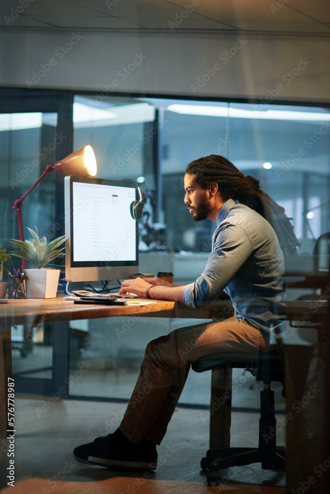 Poster Putting in the hours to achieve success. Shot of a young designer working late on a computer in an office.