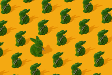 Pattern with green grass bunny toy on yellow background. Concept of Easter egg hunt. One big rabbit is antagonist.