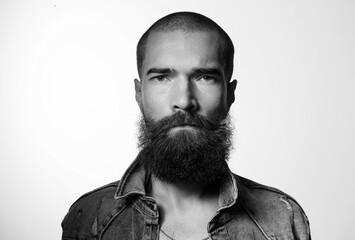 Brutal and stylish portrait of young man with beard on gray background. Artistic black and white photography. Guy with strong look and character.