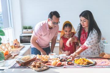Obraz na płótnie Canvas an Indian family standing in the kitchen They help each other prepare the food that they ordered. Arrange in a container placed on the table, to family and Indian food concept.