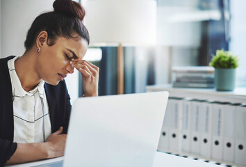 The struggle is real. Shot of a young businesswoman looking stressed while working at her desk in a modern office.