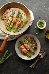 Wrapped asparagus with bacon in a frying pan and a plate. Top view