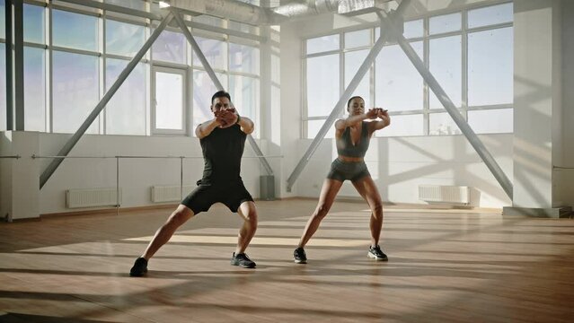 Slow motion video of a young athletic couple doing side lunges with their arms outstretched forward