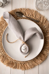 Easter composition with egg on a white plate on a white wooden table. Easter bunny napkin gift idea wrap egg
