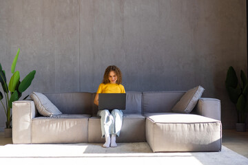Obraz premium Photo of cnice woman smiling and using laptop while sitting on couch in bright room