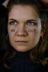 making decisions - portrait of a beautiful blonde woman with the words in and out written on her cheeks and looking away