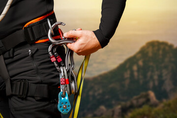 High-altitude equipment, carabiners, block rollers, on a man's belt. Telecommunications, work at height, industrial mountaineering, height, insurance. Close-up. In the mountains - obrazy, fototapety, plakaty