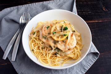 Chicken Piccata Served Over Spaghetti in a Pasta Bowl: Chicken, onions, and lemons in sauce made of garlic and white wine