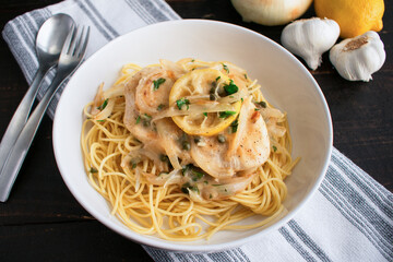Chicken Piccata Served Over Spaghetti in a Pasta Bowl: Chicken, onions, and lemons in sauce made of garlic and white wine