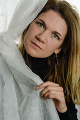 Obraz premium portrait of a beautiful blonde woman sticking out her face from white fabric and looking seriously