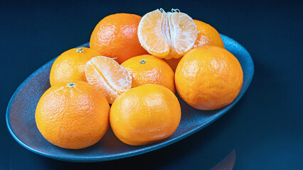 a group of ripe whole and peeled tangerines on a dark plate against a colored background