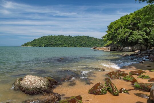 Natural landscape of Prainha in Paraty, Brazil. Sea in shades of turquoise blue, stones, strip of sand and blue sky with white clouds. In the background, the island of Ara&uacute;jo.