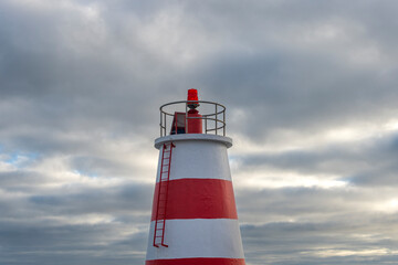 Top of a red and white lighthouse beacon against a cloudy sky.