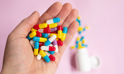 Multiple colors pills in hand on pink background. Taking Your Medication. Medicine concept.