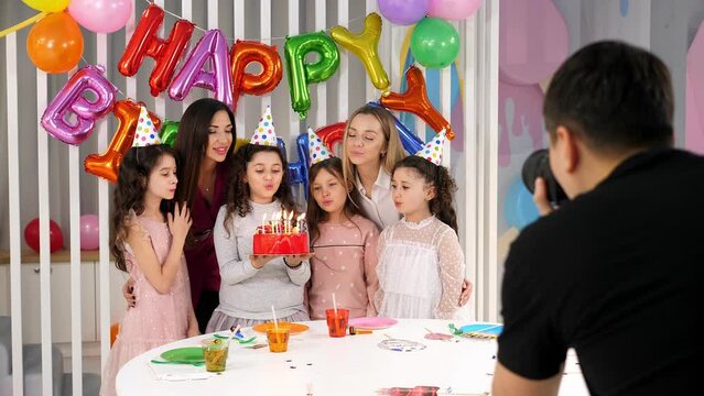 A male photographer takes pictures of a group of children and their mothers at a children's birthday party against the background of balloons.