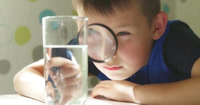 The child boy looking at water in a glass through magnifying glass
