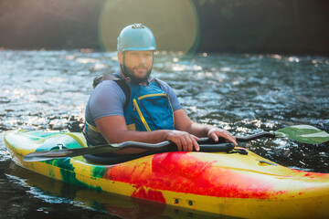 Obraz premium Caucasian man kayaking over the mountain river rapids, with the beautiful rocky bank and green forest in the background. Water sport