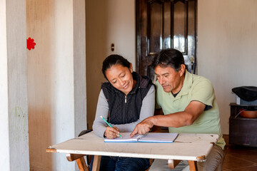 Hispanic adult couple studying together - Mayan teacher teaching senior how to write - couple budgeting at home