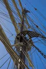 Masts, ropes, sails, ladder and hauled in sails of a historic sailing ship with a blue sky