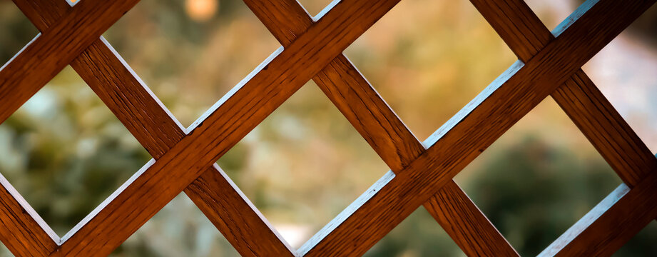 Wooden lattice, a decorative fence with garden on the background.