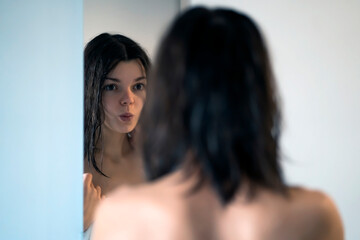 Fototapeta premium A girl in a white towel looks in the mirror and takes care of her beauty.