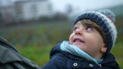 One happy little boy wearing winter clothes smiling at parent while strolling outdoors in city sidewalk