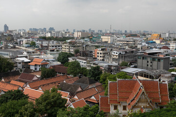 Fototapeta na wymiar Panoramic view from Golden Mount to Bangkok city. Around the orange roofs of Buddhist temples, dense tropical trees. In the distance, the gray horizon and skyscrapers of the Asian metropolis.