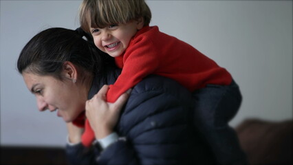 Obraz premium Little boy jumping on mother back. Authentic real life parent and child relationship laughing and smiling. Mom and kid embrace