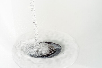 A stream of clean water pours into the white sink. Selective focus.