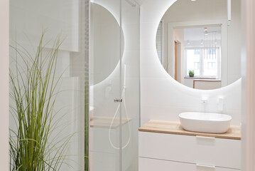 Luxury bathroom with glass to shower, round mirror with led lights, stylish washbasin and wooden...