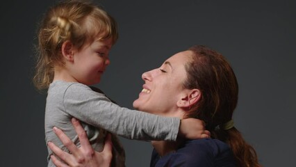 Close up shot of young mother is playing and kiss with her little girl in in a morning on gray background. Concept of children, baby, parenthood, childhood, life, maternity, motherhood