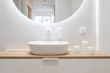 Modern bathroom with white tiles, ceramic wash basin and faucet on wooden counter with cabinet....