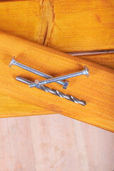 a natural yellow board is lying on a street bench. there are bolts and a drill located on it.