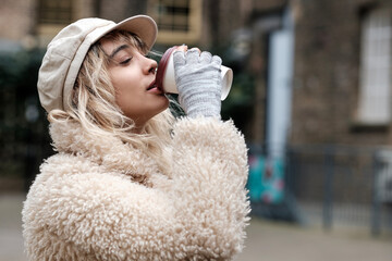 Side view of model woman drinking coffee in London street.