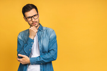 Portrait of serious fashionable handsome man in casual holding crossing hands and looking at camera isolated over yellow background.